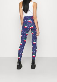 High-waisted leggings in navy with a snow globe pattern featuring green trees and red pots, accented with white snow dots. Made from stretchy material.
