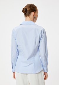 Camisa de rayas azul claro con cuello estructurado, mangas largas y puños abotonados. Tejido suave con rayas verticales y un corte ajustado.