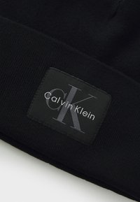 Zwart gebreid stof met een zwart rechthoekig label met het Calvin Klein-logo in grijze en witte stiksels.