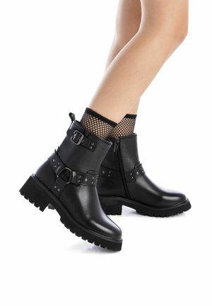 Botas negras hasta el tobillo hechas de cuero con un acabado texturizado. Las características incluyen una suela gruesa, hebillas decorativas y cierre con cremallera.