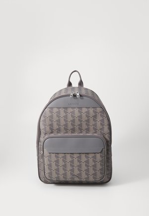 Sac à dos gris à motifs avec une finition lisse, doté d'une poche zippée sur le devant, d'une double fermeture éclair et d'une poignée sur le dessus pour le transport.