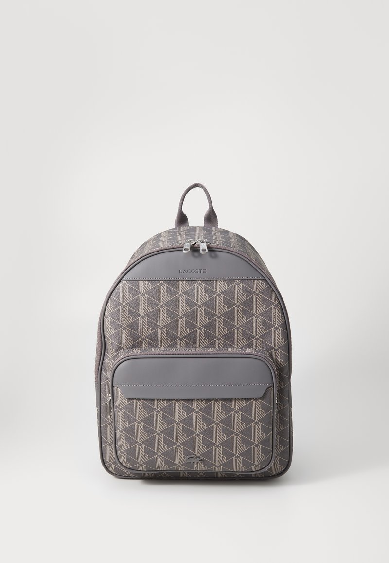 Zaino grigio a motivo con finitura liscia, dotato di tasca anteriore con zip, doppia chiusura con zip e maniglia superiore per il trasporto.