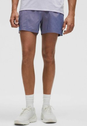 Lilla atletiske shorts lavet af letvægtsstof, med lige snit og sidelommer, parret med hvide sneakers og sokker.