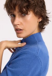 Niebieski sweter dzianinowy z prążkowanym kołnierzem, krótkimi rękawami i gładką teksturą z delikatnymi detalami na ramionach.