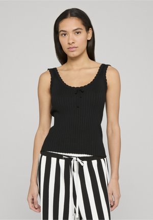 Czarny prążkowany top na ramiączkach z falowanym dekoltem i małą kokardką z przodu, zestawiony z czarno-białymi spodniami w paski.