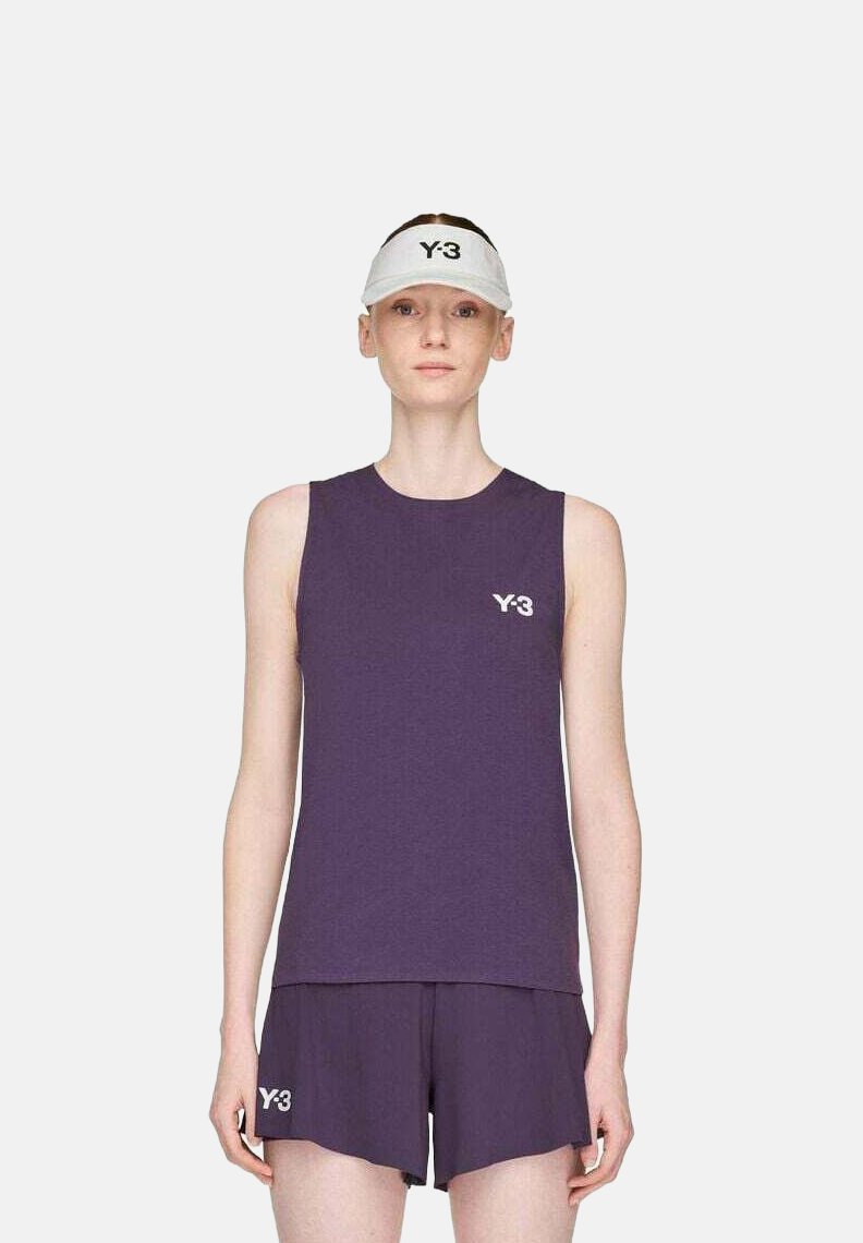 Vrouw in een paarse mouwloze top en shorts met Y-3-logo's, en een witte Y-3-zonnebril, staand tegen een effen lichte achtergrond.