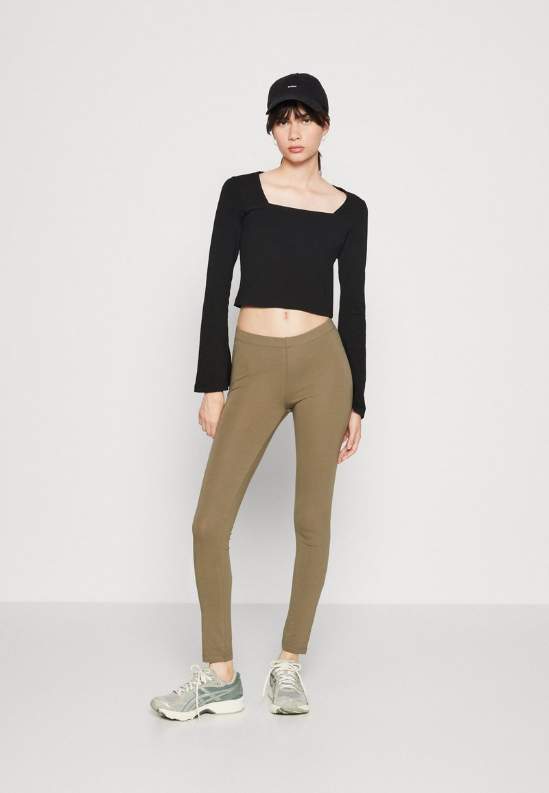 Black cropped long-sleeve top with a square neckline, paired with olive green leggings. Sneakers are grey with green accents.
