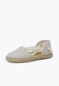 Espadrille de color beige claro con cierre de tiras cruzadas, parte superior de lona y suela de yute. Presenta una puntera redonda y ojales metálicos laterales para el cierre.