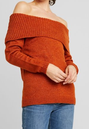 Pull en tricot orange décolleté avec un col et des poignets côtelés, présentant une texture douce et une coupe décontractée. Associé à un jean bleu.