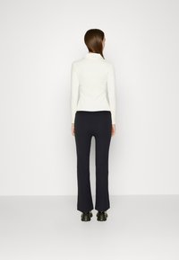 Witte blouse met lange mouwen en zwarte flared broek. De blouse heeft een kraag; de broek heeft een gladde textuur en een lichte flare aan de zoom.