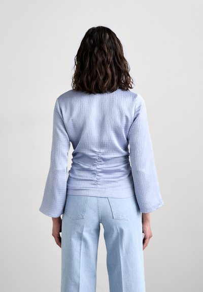Lyseblå strukturert topp med lange ermer, med en innsvinget ryggdetalj, kombinert med lyseblå høytaljede jeans.