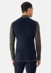 Enganliegendes Langarmshirt mit dunkelblauem Körper und olivgrünen strukturierten Ärmeln, das kontrastierende Nähte und einen hohen Kragen aufweist.