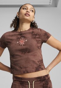 Brązowy crop top w stylu tie-dye, wykonany z miękkiego materiału, z krótkimi rękawami i haftowanym kwiatowym wzorem w kolorze różowym i białym na środku.