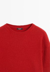 Maglione rosso lavorato a maglia con scollatura rotonda, polsini a costine e una texture morbida. Etichetta visibile all'interno del collo.