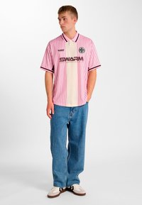 Lyserød stribet kortærmet trøje med et cremefarvet midterpanel, sorte accenter og et logo. Bæres med lyseblå løse jeans og afslappede sko.