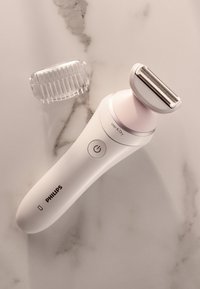 Philips elektrisch scheerapparaat in wit en roze, met een ronde handgreep, RVS mes en afneembare kamopzet op een marmeren oppervlak.
