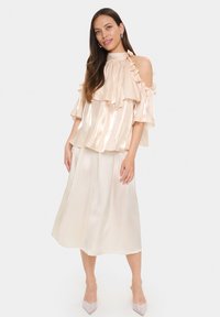 Light beige off-the-shoulder top with ruffles, paired with a flowy knee-length skirt. Smooth, shiny fabric with subtle sheen, elegant design.