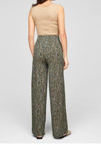 Femme portant un pantalon large à taille haute avec un motif abstrait à pois en noir, blanc et marron, associé à un haut beige sans manches à côtes.