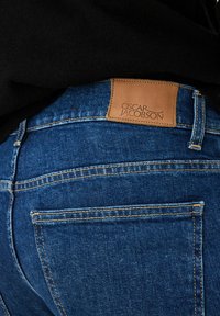 Jeans denim w ciemnoniebieskim kolorze z lekko wyblakłą fakturą. Posiadają brązową skórzaną naszywkę z napisem "OSCAR JACOBSON" w pasie.