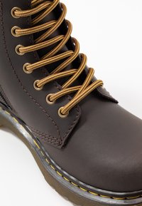 Stivale in pelle marrone con lacci gialli e marroni, occhielli dorati, cuciture gialle a contrasto e una robusta suola in gomma.