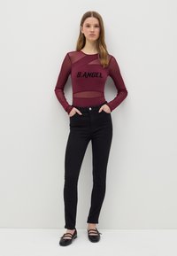 Bodysuit de malla burdeos de manga larga con el texto "B.ANGEL", combinado con jeans ajustados negros de cintura alta y bailarinas negras con tiras.