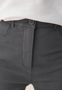 Pantalon noir en coton avec une texture lisse, présentant deux poches avant et une fermeture à bouton à la taille. Design classique et coupe ajustée.
