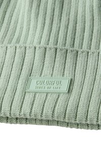 Berretto lavorato a maglia di colore verde chiaro con texture a coste verticali. Presenta un'etichetta rettangolare di colore verde menta con la scritta "COLORFUL SIDES OF LIFE" in rilievo.