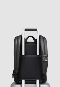 Zwarte rugzak van glad leer en gestructureerde stof, met een bovenhandvat, gewatteerde schouderbanden en een sleeve voor bagagepassage.