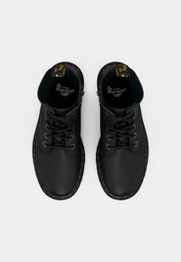 Bottes en cuir noir à lacets avec des coutures jaunes, bout arrondi et design à cheville haute. Présente un logo de la marque sur la semelle intérieure.