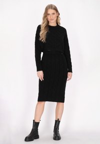 Schwarzer gerippter Strick-Crop-Pullover kombiniert mit einem passenden Bleistiftrock. Klobige schwarze Stiefel runden den Look ab. Strukturierte Zopfmuster. 