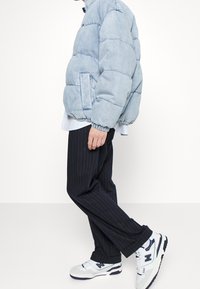 Doudoune bleu clair avec un design matelassé horizontal, associée à un pantalon à fines rayures sombres et des baskets blanches avec des accents bleu marine.