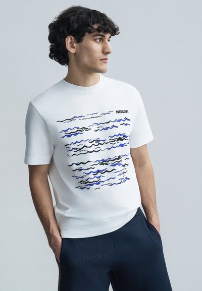 T-shirt en coton blanc avec un motif de vague en noir et bleu, avec le logo "MISSONI" imprimé en haut à gauche. Manches courtes et col rond.