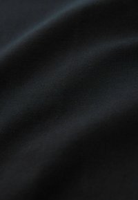 Tessuto nero con una texture liscia, superficie leggermente riflettente, che presenta morbide pieghe e un colore uniforme e costante.