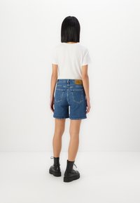 Jeanshorts med høy midje, rullet kant og to baklommer. Kombinert med en enkel hvit t-skjorte og svarte snøredestøvler.