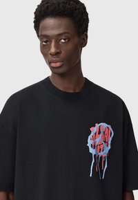 Must rebaseeritud must t-särk, millel on sinine ja punane graffiti-stiilis graafika, ümmargune disain ja tilkuvad detailid vasakus rinnapiirkonnas.