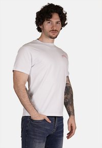 T-shirt in cotone bianco con maniche corte, colletto rotondo e piccolo logo rosa sul petto, abbinato a jeans in denim blu scuro.