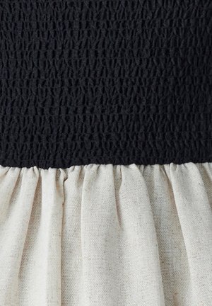 Black textured fabric on top with a gathered cream linen ruffle at the bottom. The materials exhibit contrasting colors and patterns.