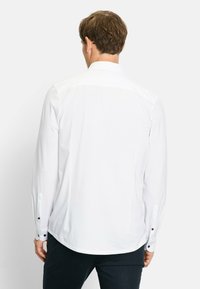 White long-sleeve shirt with a buttoned collar, featuring black buttons on the cuffs and a smooth texture. The shirt is neatly tucked.