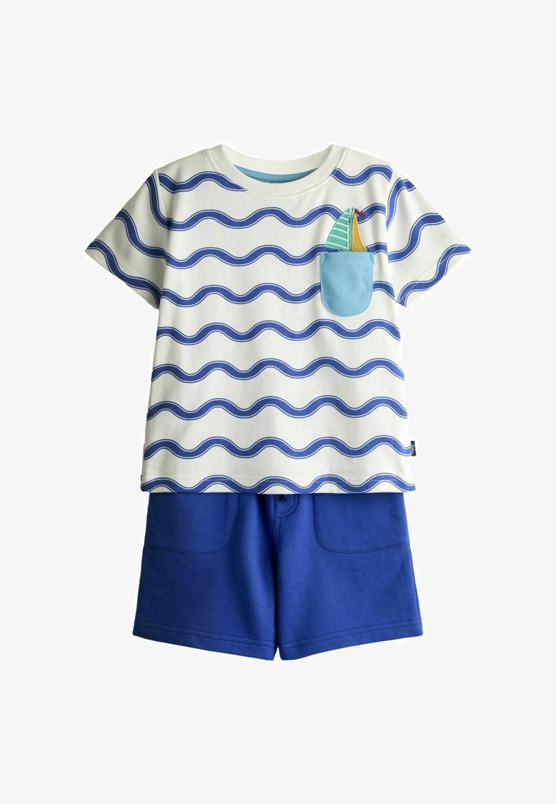 Tenue pour tout-petit avec une chemise blanche à manches courtes ornée de rayures ondulées bleues et un voilier dans la poche poitrine, accompagnée d'un short bleu uni.