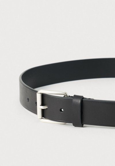 Μαύρη δερμάτινη ζώνη με λεία υφή, που διαθέτει ασημί μεταλλικό αγκράφα και οπές διάσπαρτες κατά μήκος του ιμάντα για ρύθμιση.