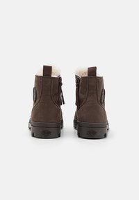 Bottes chevilles en cuir marron avec doublure en fausse fourrure, une surface texturée et des languettes. Elles possèdent une semelle en caoutchouc et un logo de marque sur le côté.