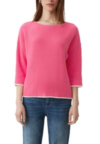 Rosa gestrickter Pullover mit 3/4-Ärmeln, der eine gerippte Textur und kontrastierende weiße Abschlüsse am Ausschnitt und Saum aufweist. Getragen mit blauen Jeans.