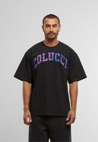 Černé oversized tričko s nápisem "COLUCCI" v barevných, texturovaných písmenech. Krátké rukávy a volný střih zvyšují pohodlí a styl.