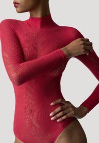 Body in rete rosso con collo alto e maniche lunghe, caratterizzato da motivi intricati e una silhouette aderente, che mette in mostra la pelle sotto il tessuto.