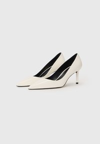 Beli lakirani čevlji z ozkim nosom in elegantnim dizajnom, s srednje visokim stiletto peto in kontrastno črnino notranjosti.