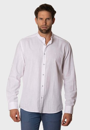 Camisa blanca de manga larga con cuello alto, cierre de botones y una textura sutil; presenta un pequeño logo en el pecho. Llevada con pantalones azules.
