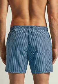 Bañador de hombre en azul con rayas verticales blancas. Cintura elástica, bolsillo trasero con cierre de botón y tejido transpirable.