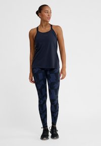 Marinblå linne med tunna axelband, kombinerat med mönstrade marinblå leggings med abstrakta former i olika nyanser av blått, bärs med svarta skor.