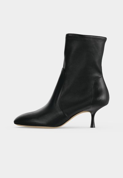 Bottine en cuir noir avec bout pointu et talon fin de hauteur moyenne, vue de profil sur fond clair.