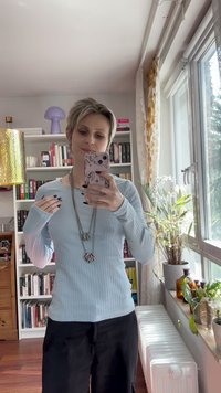 Lyseblå ribbet langermet topp kombinert med svarte bukser. Iøynefallende sølvsmykke med skjellformede anheng. Naturlig lysmiljø.